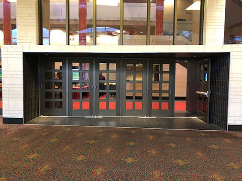 This photo shows a white marble entrance that juts into the hallway. There are black French-style doors leading to the Lila Cockrell Theatre lobby. Directly before the doorway is black tile.